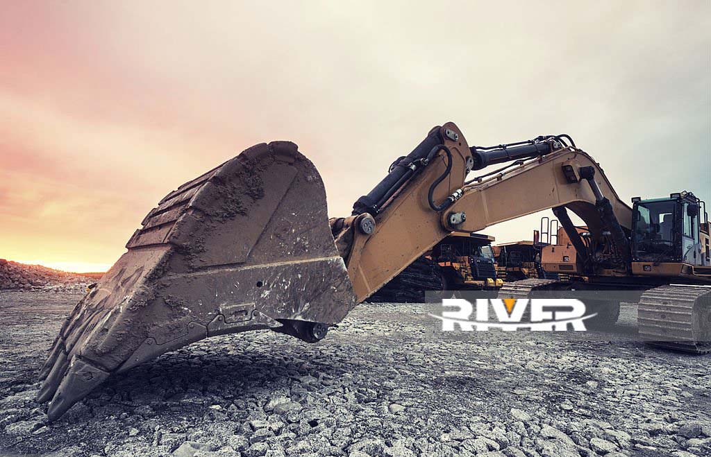 A large excavator on a construction site under sunset skies.